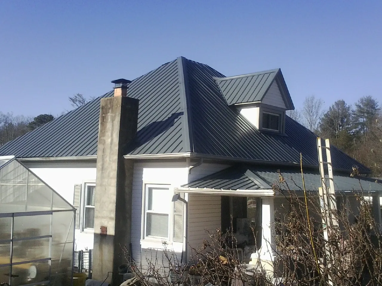 Dark blue standing seam metal roof on a white farmhouse with dormer — Slate & Tile Roof Repair by Roofing Brothers in Herman