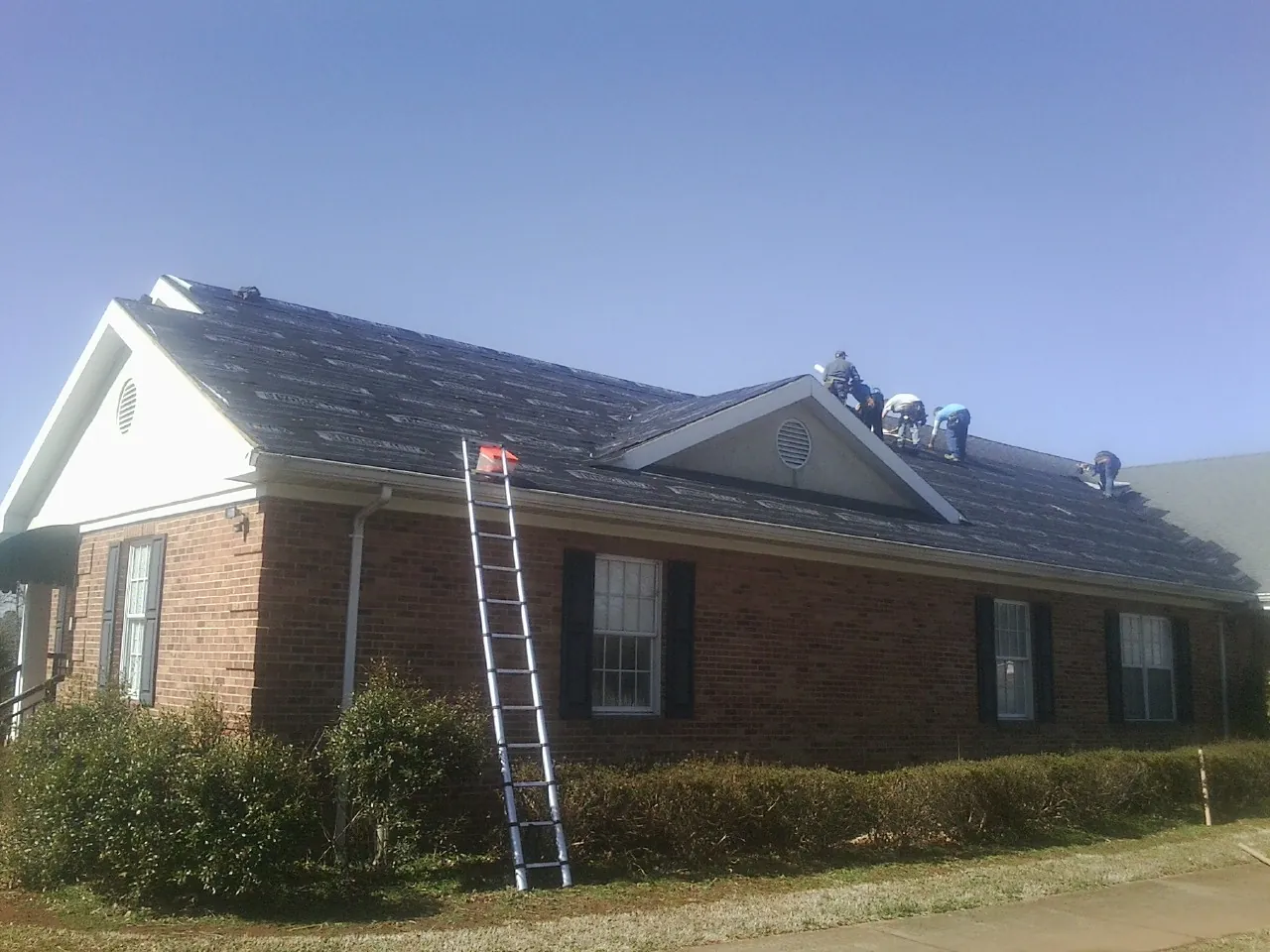 Crew tearing shingles off a brick ranch roof with a ladder set — Emergency Roof Repair work by our crew in Herman